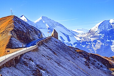The famous panoramic mountain road Grossglocknerstrasse. Snow-capped mountain peaks are covered with clouds. Stone lookout tower at a sharp turn