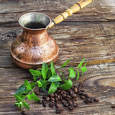 Vintage copper Turk on wooden background covered coffee beans with mint petals