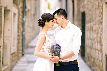 Sibenik, Croatia - 05.06.17: Groom leaned his forehead against the bride's forehead with a lavender bouquet in a white dress against the background of an old city street