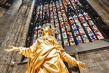 Statue of Madonna in gold against the background of a stained glass window in the Duomo. Milan, Italy.