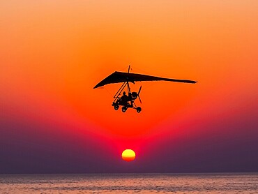 The person flying on a trike with the motor against The hang-glider is flying against the sunset