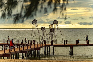 Families walking on a pier with jellyfish sculptures at a peaceful ocean sunset, sun, sunset, beach, sand, sculpture, clouds, Sunset Sanato Beach in Phu Quoc island in Vietnam