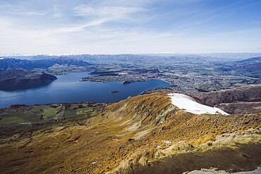 Landscape with a sweeping view of a lake, a valley and a distant town, Roys Peak, Wanaka, New Zealand, Oceania