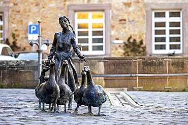 Statue of a girl with geese in front of a historic building, a parked car in the background, The Gänseliesel monument in Melsungen