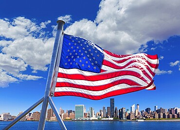 The skyline of Manhattan shines brightly over the East River with a flag