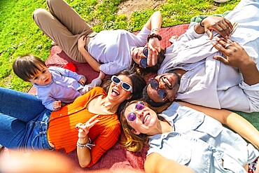 Group of cheerful multi ethnic friends enjoying a sunny day at the park taking a selfie while lying on a blanket