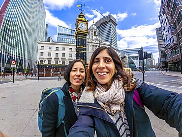 Two happy tourists taking a selfie with a fisheye lens in front of a historic clock tower in london, uk, capturing their travel adventure