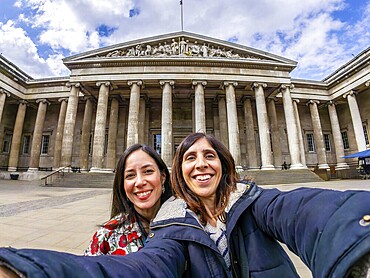 Two happy female tourists are taking a selfie with a fisheye lens in front of the british museum in london