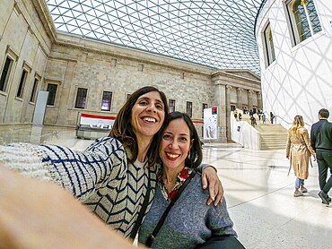 Two joyful female tourists capturing a selfie while enjoying their time in the stunning great court of the british museum in london