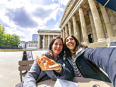 Two happy female tourists taking a selfie with fisheye lens in front of the british museum in london, uk