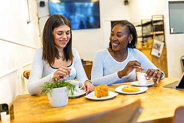 Two young women enjoying a coffee break, chatting and laughing together in a vibrant, modern cafe filled with natural light