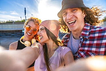 Three cheerful young friends taking a selfie outdoors, soaking up the sun and enjoying a vibrant day in the city together