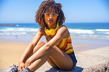 Fashionable young woman enjoying the summer sun and music on a beach wall, embracing the carefree vibes of vacation