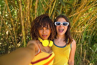 Two cheerful female friends capturing a joyful selfie while enjoying their vacation in a lush bamboo forest, surrounded by vibrant greenery