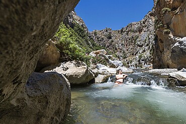 Preveli Beach, at the end of the Kourtaliotiko Gorge, South Coast, Crete, Greek Islands, Greece, Europe. young man sitting in the river, Europe