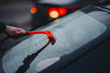 Someone uses an orange scraper on a car's rear window