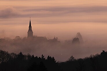 Wisps of mist drift into the town of Kronberg in Taunus in the morning shortly in front of sunrise. Only the spire of St Peter and Paul's Church stands out. Kronberg, Malerblick, Hesse, Germany
