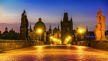 Charles Bridge illuminated with street lights at sunrise, Prague