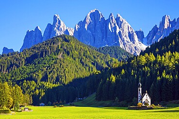 Small white church with among green lawns on the sunset. The village Santa Maddalena in the Val di Funes Valley. Italy, Tyrol. The concept of active, ecological and photo tourism