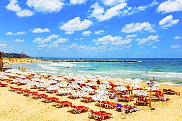 Mediterranean Sea. The magnificent modern city of Tel Aviv. Comfortable red sun loungers for tourists. Multicoloured umbrellas protect from the hot sun. Sunny day on a beautiful beach