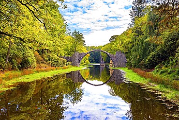 The Devil's Bridge on the Rakots River. Park Kromlau, Germany. The basalt columns of the bridge form a perfect circle with their reflection in the water. Picturesque narrow bridge in the park