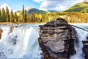 Magnificent rock divides thundering Athabasca Falls. Athabasca Falls is the most powerful waterfall in Alberta. Jasper Park. Canadian Rockies. Picturesque forest illuminated by sunset