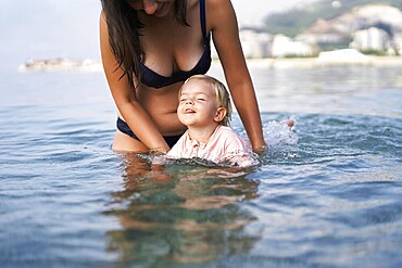 Mom teaches a little girl to swim in shallow water.