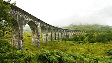 High resolution panorama of Glenfinnan railway viaduct (location from Harry Potter movie) shot from side, on overcast day with grey sky and lot of green grass and trees around. Inverness, Scotland, United Kingdom