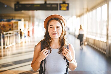 Theme tourism travel. Young beautiful Caucasian woman in dress and hat with backpack tourist mat in terminal station in a long walkway, the schedule board, the gate of the departure and the plane