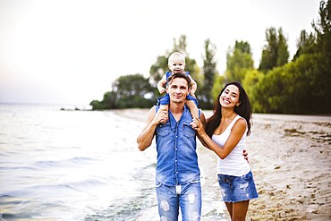 Beautiful young family on holiday with baby. The father holds the blonde girl in her arms, and the brunette's mother hugs her husband. The concept of a family beach holiday summer near the sea