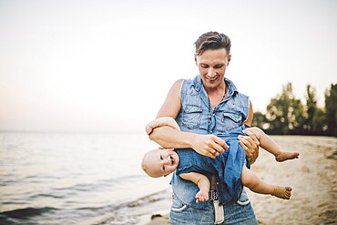 Theme Fatherhood and rest with a child at sea. Young handsome Caucasian father plays plays enjoys throwing up in arms his child up in summer daughter on the sandy beach on the seashore