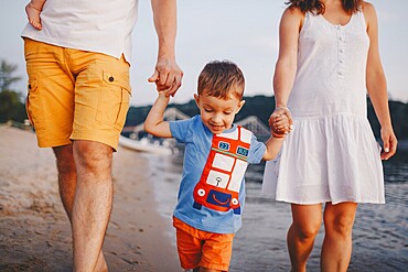Family holiday in summer. Young Caucasian family foot walking barefoot sandy beach, shore river water. Dad mom holding hands two children, brothers. Big friendly family with two children near lake