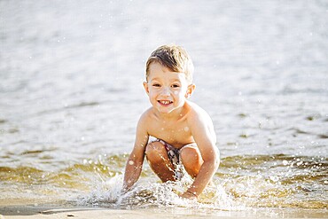 Theme is summer time and rest near the water. Little joyful Caucasian funny boy plays and enjoys in the river. The child is resting and swimming in the lake pond sandy beach