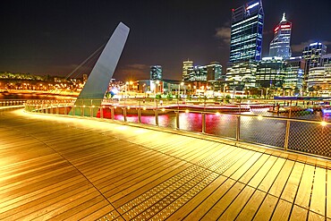 Wooden walkway of Elizabeth Quay pedestrian bridge illuminated by night at Elizabeth Quay marina, a new tourist attraction in Perth, Western Australia. Esplanade on background. Night scene, Perth, Australia