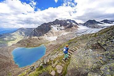Mountaineer on hiking trail in front of dramatic high mountain landscape, view of mountain lake Vogelhüttensee and glacier Übeltalferner, Stubai Alps, South Tyrol, Italy