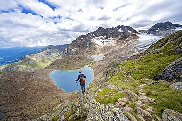 Mountaineer in front of dramatic high mountain landscape, view of mountain lake Vogelhüttensee and glacier Übeltalferner, Stubai Alps, South Tyrol, Italy