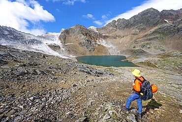 Mountaineer in front of mountain landscape with limestone rocks between granite mountains, mountain lake Hinterer Senner Egetsee and mountain peak of the Moarer Weißen, Seven Lakes Hike, Stubai Alps, near Ridnaun, South Tyrol, Italy
