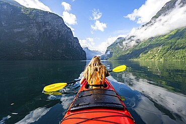 Kayak trip on the Geirangerfjord, young woman paddling in a red kayak, atmospheric fjord landscape, Møre og Romsdal, Norway