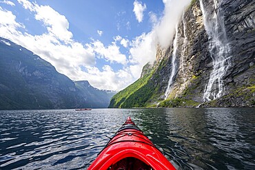 Kayak trip on the Geirangerfjord at the waterfall The Seven Sisters, tip of a red kayak in the fjord, atmospheric fjord landscape, first person view, near Geiranger, Møre og Romsdal, Norway