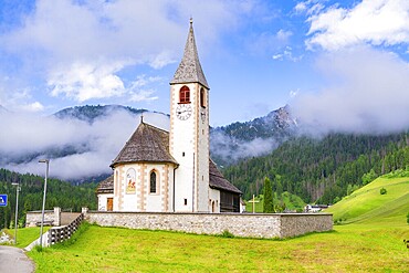 Church with tower and clock, surrounded by meadows and mountains in an alpine landscape, Dolomites, South Tyrol, Italy