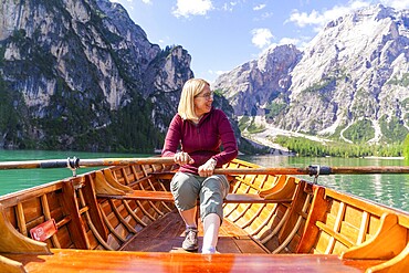 Smiling woman rowing in a boat on a mountain lake in sunny weather, Lake Braies, South Tyrol, Dolomites, Italy