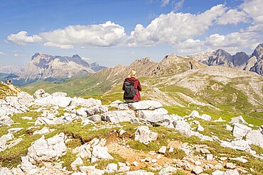 Person sitting on rock with rucksack, mountain panorama and blue sky in the background, hike to Schlehrn, Alpe di Siusi, Dolomites, South Tyrol, Italy