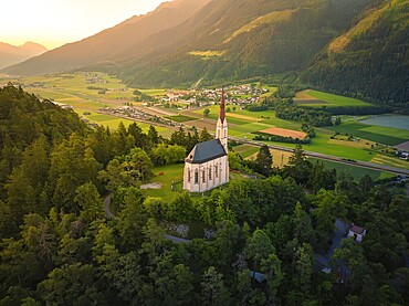 View from a hill with a church over a wide valley at sunset