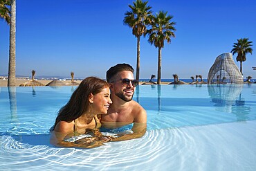 Tourist couple having bath in infinity pool on a beach resort in summer vacation