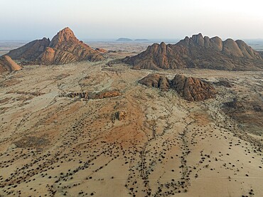 Spitzkoppe (1728 m) - on the left - and Pondok Mountain majestically rise above the surrounding desert plains. At dawn. Aerial view. Drone shot. Damaraland, Namibia