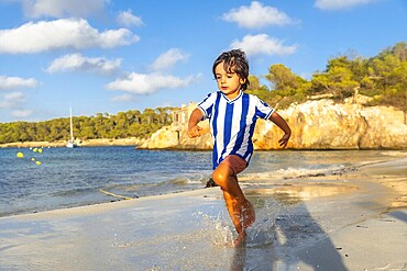 Happy child running on the wet sand of s'amarador beach in mallorca, Spain, during summer holidays, enjoying the beautiful mediterranean sea