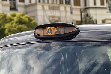 Illuminated taxi sign on top of a classic black cab in London, England, providing transportation services in the urban environment