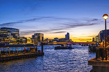 Tugboats sailing on thames during sunset with London’s illuminated skyline reflecting on the water