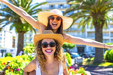 Two cheerful female friends are having fun during summer vacation, wearing sunglasses and straw hats
