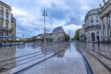 Comedie square in bordeaux city centre with wet tram tracks reflecting surrounding buildings on a cloudy morning